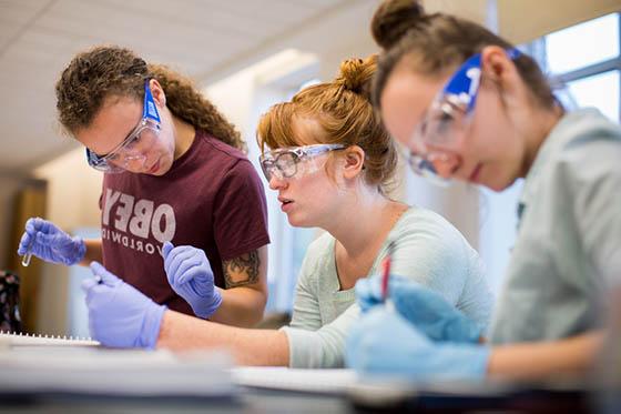 图为三名2024欧洲杯官方投注的女学生戴着护目镜和手套在实验室工作